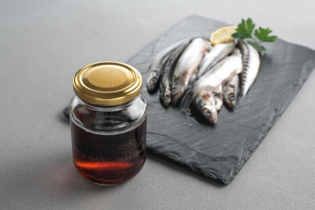 Un pot en verre de sauce de poisson à côté de plusieurs petits poissons.