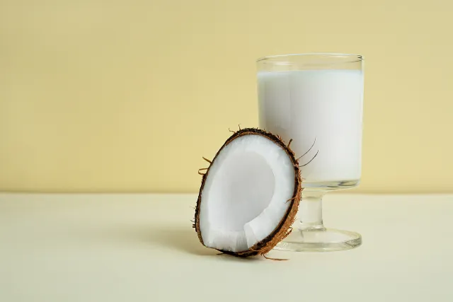 Un verre de lait de coco à côté d'une demi-noix de coco.