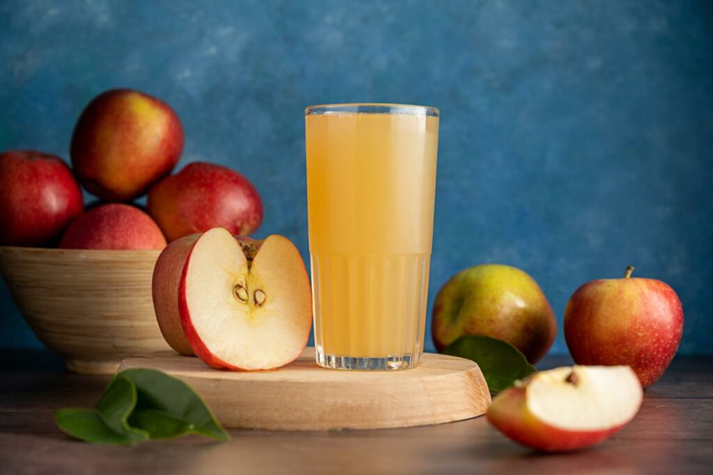 Un verre de jus de pomme trouble entouré de pommes fraîches.