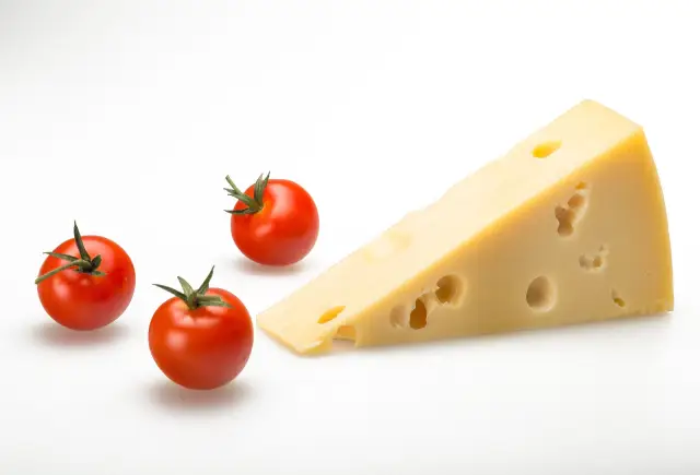 Un morceau d'Emmental à côté de quelques tomates cerises.